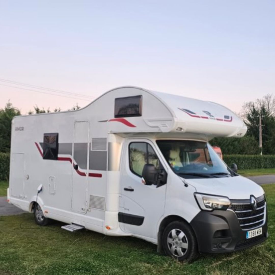 Autocaravana perfilada moderna de color blanco aparcada en zona de césped al atardecer.