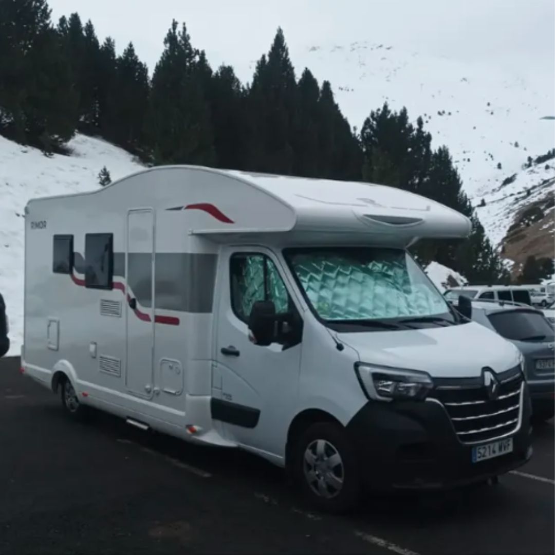 Autocaravana blanca aparcada en un entorno de montaña nevada.