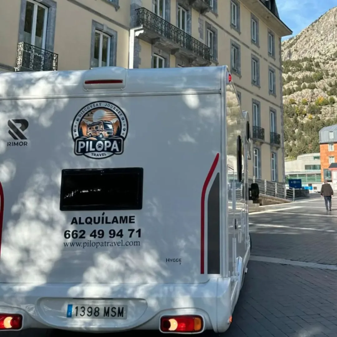 Parte trasera de autocaravana con logo de empresa de alquiler y matrícula visible en entorno urbano.